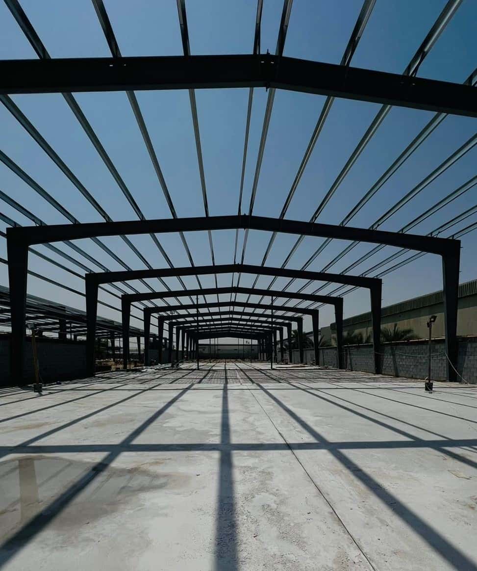 Symmetrical steel portal frames of a warehouse casting shadow lines across the concrete slab